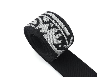 May include: Black and white patterned webbing with a silver design. The webbing is rolled up and the end is hanging down.
