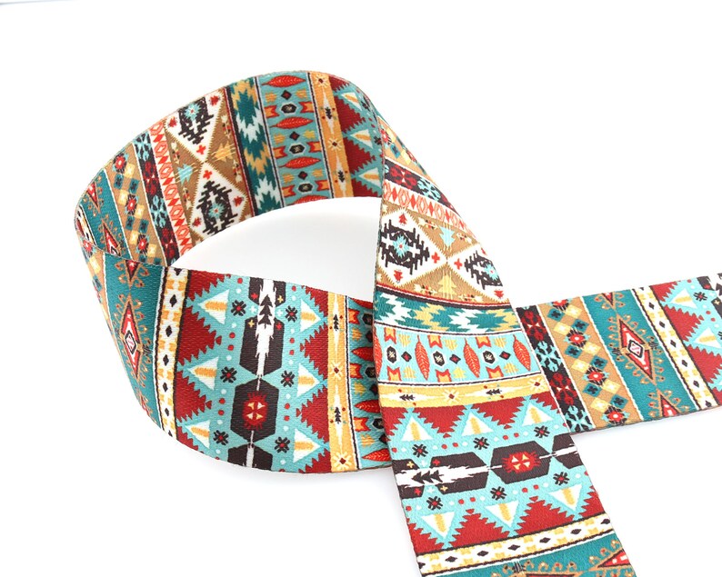 Op de afbeelding: Een geweven gitaarband met een kleurrijk geometrisch patroon in tinten van teal, rood, bruin en goud.