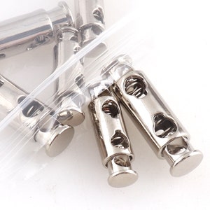 Puede incluir: Primer plano de organizadores de cables de metal plateado con mecanismos de resorte. Los organizadores están diseñados para sujetar y asegurar los cables.