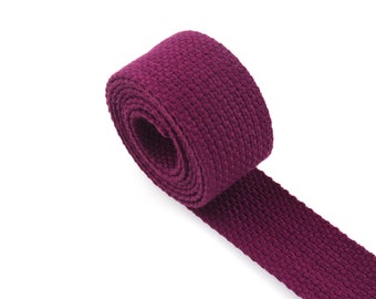May include: A roll of deep purple cotton webbing, a type of flat, woven fabric often used for straps, belts, and other craft projects.