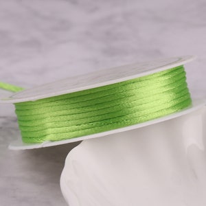 May include: A spool of bright green satin ribbon wound around a white plastic spool. The ribbon is smooth and shiny.