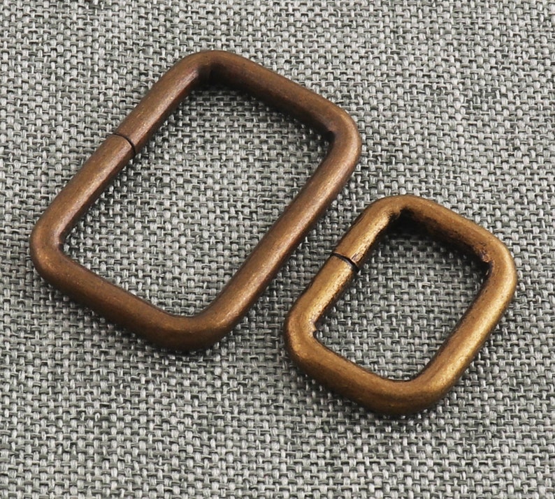May include: Two antique gold-toned metal D-rings. The larger ring is about 5 cm long and the smaller ring is about 2.5 cm long.