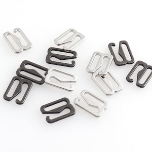 Op de afbeelding: Een verzameling bh-bandjesverstellers in zilver en zwart. De metalen verstellers hebben een rechthoekige vorm met een haak aan één uiteinde en een lus aan de andere kant. De verstellers zijn verspreid op een witte achtergrond.