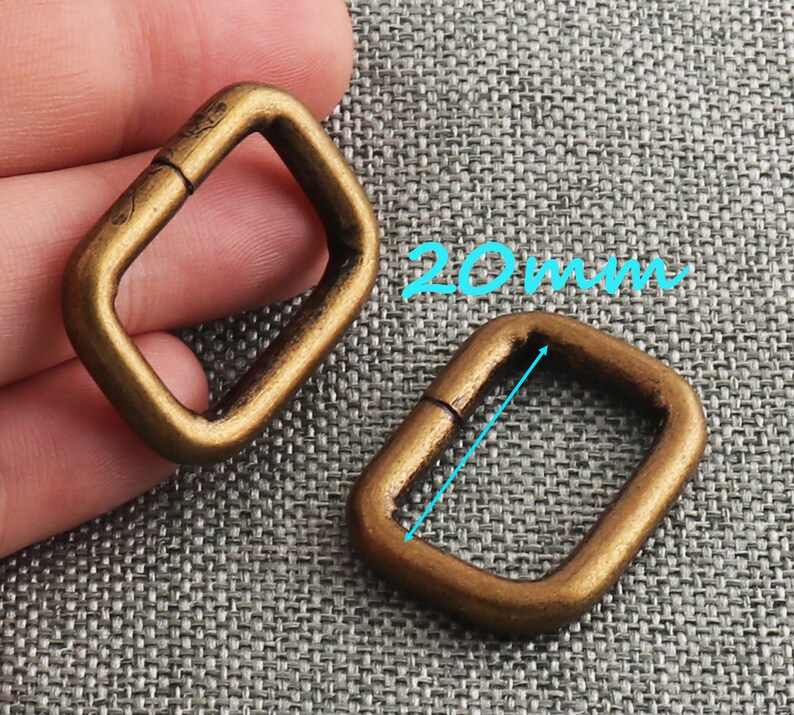 May include: Two gold-toned metal D-rings, each measuring 20 mm in length. The rings are open and have a smooth, polished finish.