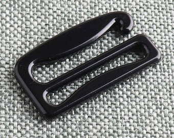 May include: Black plastic bra strap slider. The slider has a hook on one end and two loops on the other end.