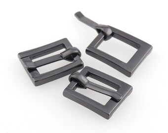 Puede incluir: Tres hebillas de cinturón de metal negro. Las hebillas son rectangulares con un acabado liso y brillante.