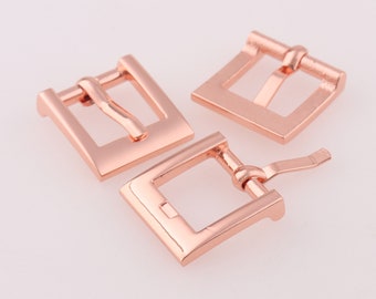 Puede incluir: Tres hebillas de correa de reloj de metal de color oro rosa. Las hebillas son rectangulares con un acabado liso.