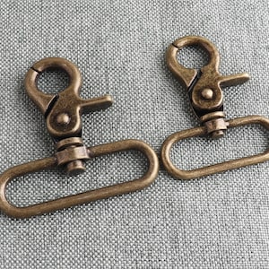 Puede incluir: Dos cierres giratorios de metal de color dorado antiguo con un bucle rectangular. Los cierres son de diferentes tamaños.