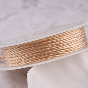 May include: A spool of beige satin cord, wound tightly and ready for crafting projects.