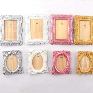 May include: Eight decorative picture frames in a variety of colours, including silver, white, pink, and gold. The frames have ornate edges and hold a wooden backing. Some are rectangular, others oval.