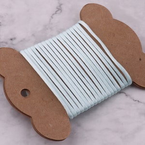 May include: A spool of light blue cord wound around a brown cardboard bear-shaped holder.