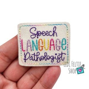 May include: A white glitter patch with the text "Speech Language Pathologist" embroidered in rainbow colors.