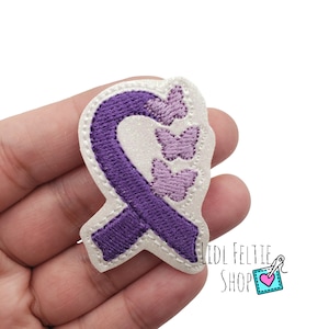 May include: Purple ribbon with three purple butterflies on a white felt background. The ribbon is a symbol of awareness for many causes.