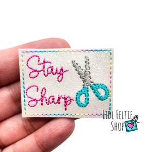 May include: White glitter iron-on patch with pink embroidery that says "Stay Sharp" and a pair of teal scissors.
