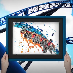 Könnte beinhalten: Ein gerahmtes Kunstwerk, das eine Achterbahn in Aktion zeigt, mit einer blauen Strecke und farbenfrohen Spritzern in Orange und Blau. Das Kunstwerk wird vor dem Hintergrund einer blauen Achterbahnstruktur und eines teilweise bewölkten Himmels präsentiert.
