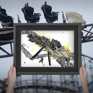 May include: A framed artwork depicting a roller coaster in a watercolor style, held in front of a real roller coaster. The artwork features black and yellow accents, with the coaster's structure and cars visible.