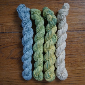 May include: Four skeins of yarn in different shades of blue, green, and white. The yarn is twisted into a rope shape.