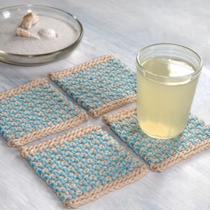 May include: Four knitted coasters in beige and blue with a glass of lemonade on top of one of the coasters.