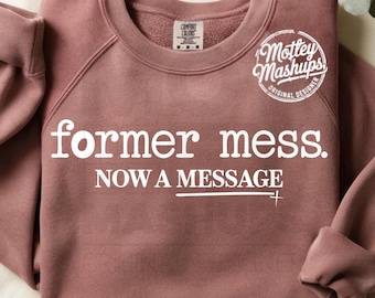 Może przedstawiać: Bluza w kolorze malwy z białym napisem "former mess. NOW A MESSAGE". Bluza z okrągłym dekoltem ma długie rękawy i okrągłe logo z napisem "Mottey Mashups, Original Designer".
