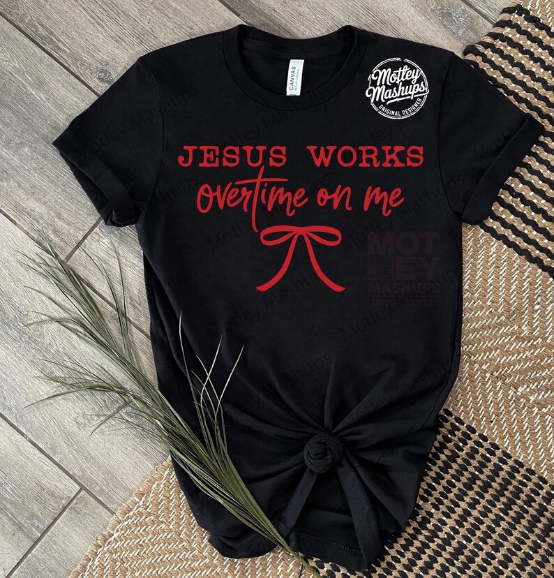 May include: Black t-shirt featuring the red text "JESUS WORKS overtime on me" and a red bow graphic. The shirt is knotted at the hem. The brand logo "Motley Mashups" is in the upper right corner.