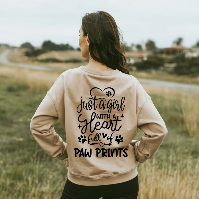 May include: A tan sweatshirt with the text "just a girl with a heart full of paw prints" in black lettering. The text is surrounded by paw prints and hearts.