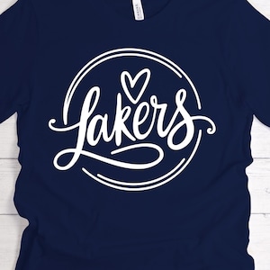 May include: Navy blue t-shirt with a white graphic. The graphic features the word "Lakers" in a cursive font, encircled by a double white line, with a heart symbol above the "a". The shirt is made of a soft material.