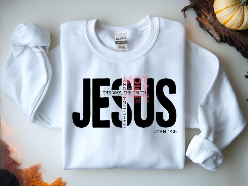 May include: White sweatshirt with the word "JESUS" in large black letters. The words "NOT" and "THE WAY, THE TRUTH, THE LIFE" are in a smaller, pink font. The text "JOHN 14:6" is at the bottom in black.
