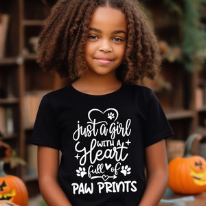 May include: A young person wearing a black t-shirt with white text that reads "Just a girl with a heart full of paw prints".