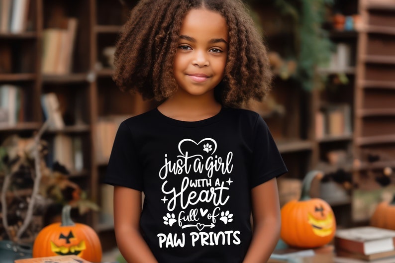 May include: A young person wearing a black t-shirt with white text that reads "Just a girl with a heart full of paw prints".