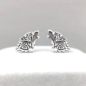 May include: A pair of silver earrings featuring a detailed wolf head design. The wolf's mouth is open and the ears are pointed.