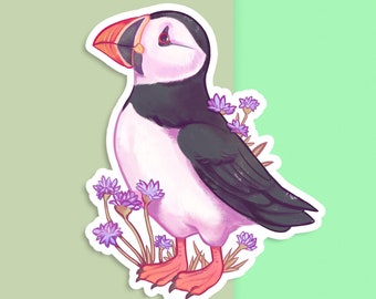 May include: A sticker featuring a cartoon illustration of a puffin with a black and white body, orange beak, and pink feet. The puffin is surrounded by purple flowers.