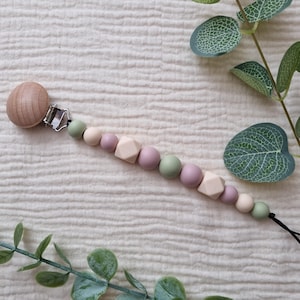 May include: A dummy clip featuring a round wooden bead, a silver metal clasp, and a string of silicone beads in alternating shades of sage green, cream, and dusty rose, including two geometric cube-shaped beads, arranged on a cord.