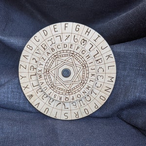 以下が含まれることがあります： 円形のデザインと中央の星を持つ木製暗号ホイール。ホイールは、アルファベットの文字とエッジの周りの数字を持つ回転する外側のリングを持っています。