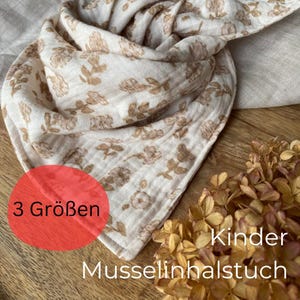 Op de afbeelding: Een witte muslin-wikkeldoek met een bruin bloemenpatroon. De wikkeldoek is gevouwen in een driehoekige vorm en heeft de tekst "3 Größen" op een rode cirkel. De tekst "Kinder Musselinhalstuch" is zichtbaar onderaan de afbeelding.