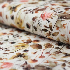Op de afbeelding: Witte stof met een aquarelpatroon van bruine en oranje bloemen en bladeren.