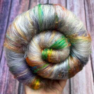 May include: A tightly wound skein of colorful yarn. The yarn is a mix of gray, white, green, orange, yellow, and purple fibers. The fibers are soft and fluffy, with a slight sheen. The yarn is likely used for knitting or crocheting projects.