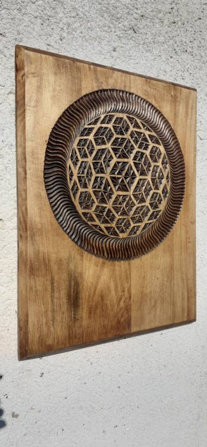 K&ouml;nnte beinhalten: Ein Wandbehang aus Holz mit einem geschnitzten geometrischen Muster in der Mitte. Das Muster ist dunkelbraun und von einem hellbraunen Holzrahmen umgeben.