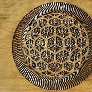 K&ouml;nnte beinhalten: Ein Holztablett mit einem geschnitzten geometrischen Muster in der Mitte. Das Muster ist eine Kugel mit einem sich wiederholenden Muster aus Sechsecken und Dreiecken. Das Tablett ist aus hellbraunem Holz gefertigt und hat eine dunkelbraune Beize.