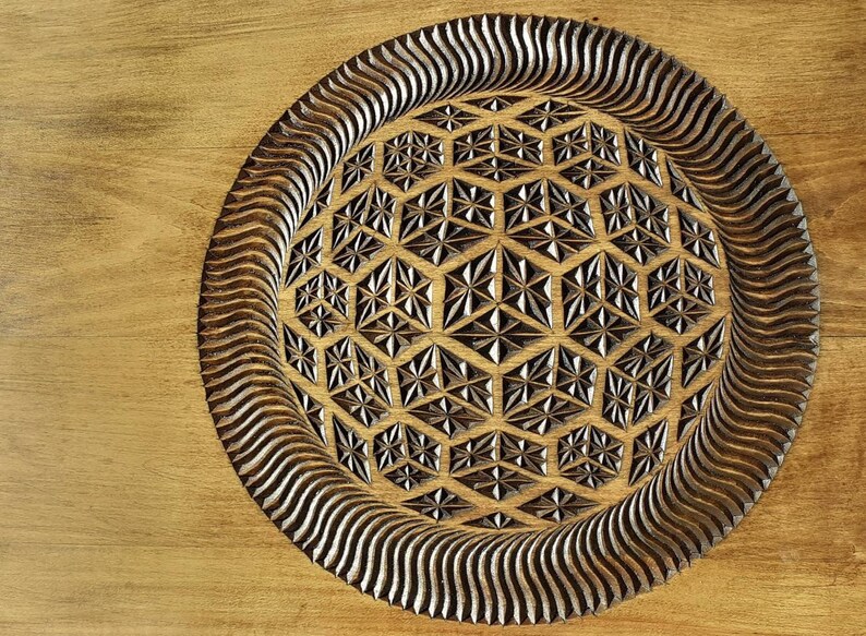 K&ouml;nnte beinhalten: Ein Holztablett mit einem geschnitzten geometrischen Muster in der Mitte. Das Muster ist eine Kugel mit einem sich wiederholenden Muster aus Sechsecken und Dreiecken. Das Tablett ist aus hellbraunem Holz gefertigt und hat eine dunkelbraune Beize.