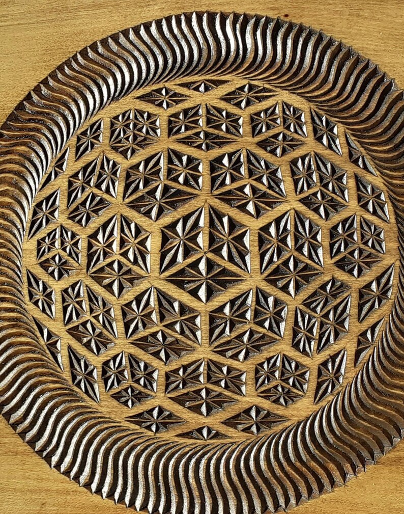 K&ouml;nnte beinhalten: Ein rundes Holztablett mit einem geschnitzten geometrischen Muster in der Mitte. Das Muster ist ein sich wiederholendes Design aus Sternen und Diamanten. Das Tablett hat eine dunkelbraune Beize und eine nat&uuml;rliche Holzoptik.