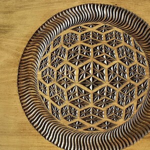 K&ouml;nnte beinhalten: Ein Holztablett mit einem geschnitzten geometrischen Muster in der Mitte. Das Muster ist ein kreisf&ouml;rmiges Muster aus sich wiederholenden Sechsecken und Sternen. Das Tablett ist aus hellbraunem Holz gefertigt und hat eine nat&uuml;rliche Oberfl&auml;che.