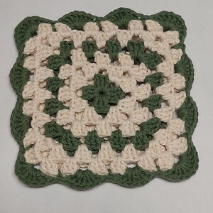 May include: A crocheted square coaster with a green and cream color pattern. The coaster has a scalloped edge.