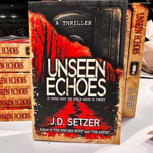 May include: A stack of books with the title "Unseen Echoes" by J.D. Setzer. The cover features a dark, ominous design with red trees and a road. The text "A Thriller" is at the top.