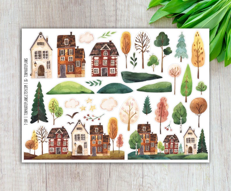 May include: A sticker sheet featuring watercolor illustrations of houses, trees, clouds, and other landscape elements. The houses are in various styles with brown, orange, and white facades. The trees display green, yellow, and brown foliage. The text "T-187 | TINYKATEPLANS.ETSY.COM" is visible.
