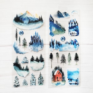 May include: A sheet of clear stickers with watercolor illustrations of winter scenes. The stickers feature mountains, trees, a cabin, and a moon. The stickers are perfect for adding a touch of winter magic to your planner, journal, or scrapbook.