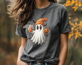 Puede incluir: Una camiseta gris con un fantasma de dibujos animados que lleva una boina naranja y sostiene una calabaza y una taza de líquido naranja. El fantasma tiene una cara amigable y está rodeado de murciélagos.