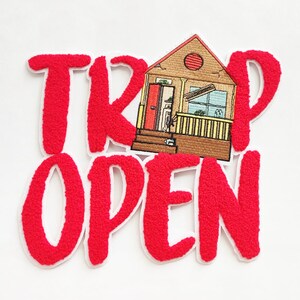 Puede incluir: Parche bordado rojo con las palabras "Trap Open" y una imagen de dibujos animados de una casa con una puerta roja y un porche amarillo.