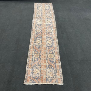 Könnte beinhalten: Ein langer, schmaler Teppich mit traditionellem persischem Design. Der Teppich hat einen dunkelblauen Hintergrund mit komplizierten floralen Mustern in Beige-, Orange- und Rottönen.