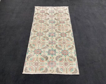 May include: A vintage cream-colored rug with a floral pattern in shades of pink, teal, and brown. The rug has a fringed edge and is approximately 2 feet wide and 6 feet long.