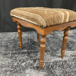 May include: A wooden stool with a brown and white striped fabric seat. The stool has four turned legs and a carved design on the top.